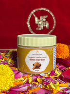Open jar of sandalwood powder surrounded by marigold and rose petals