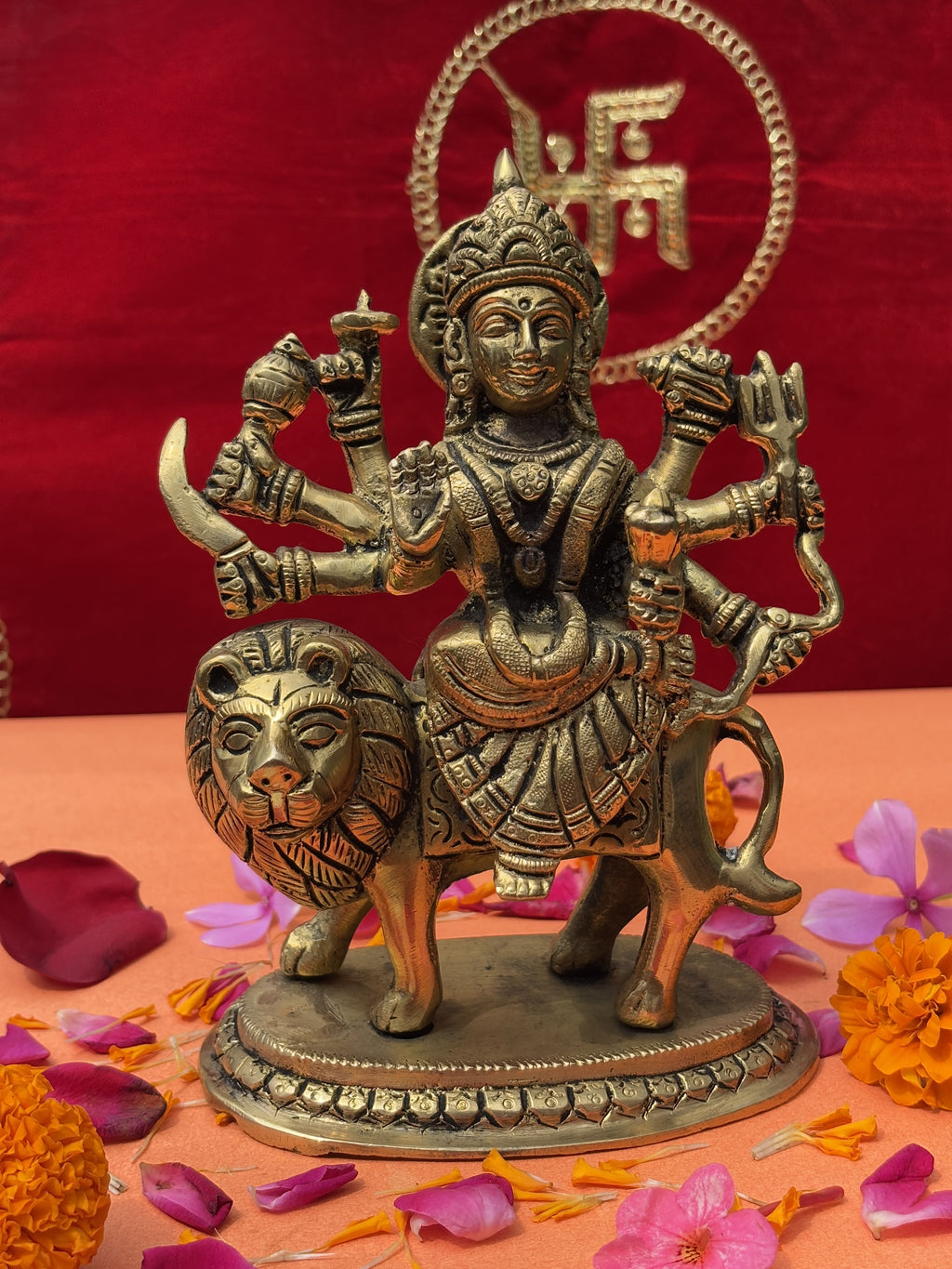 Antique brass statue of Maa Durga with multiple arms, lion mount, and Swastik backdrop