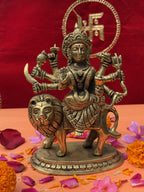 Antique brass statue of Maa Durga with multiple arms, lion mount, and Swastik backdrop