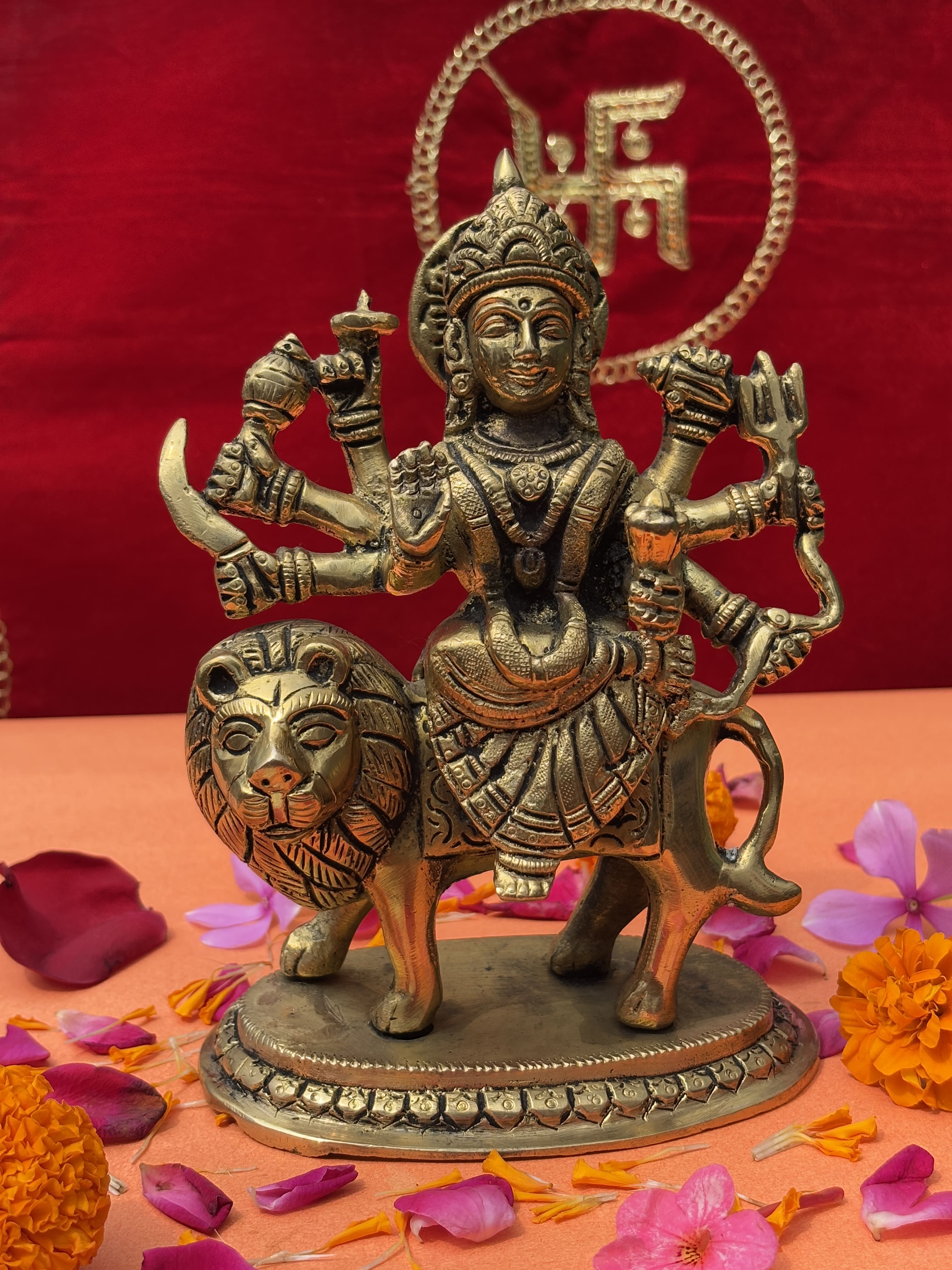 Antique brass statue of Maa Durga with multiple arms, lion mount, and Swastik backdrop